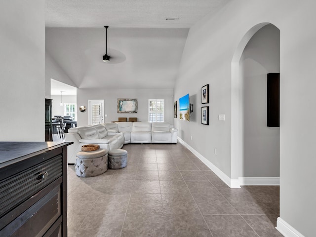 living area with arched walkways, high vaulted ceiling, baseboards, and dark tile patterned flooring