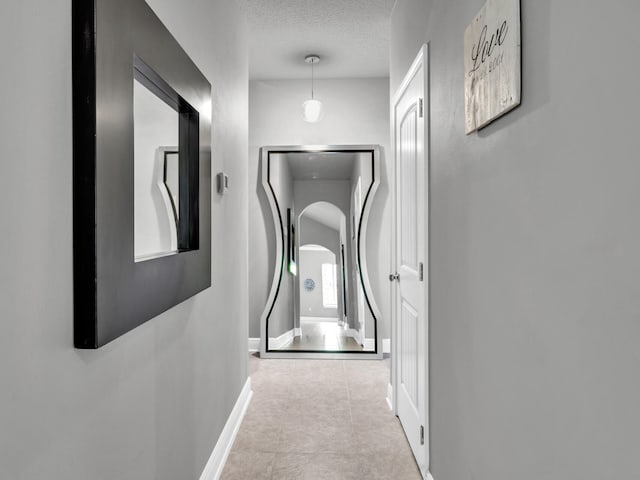 corridor with a textured ceiling, tile patterned flooring, and baseboards