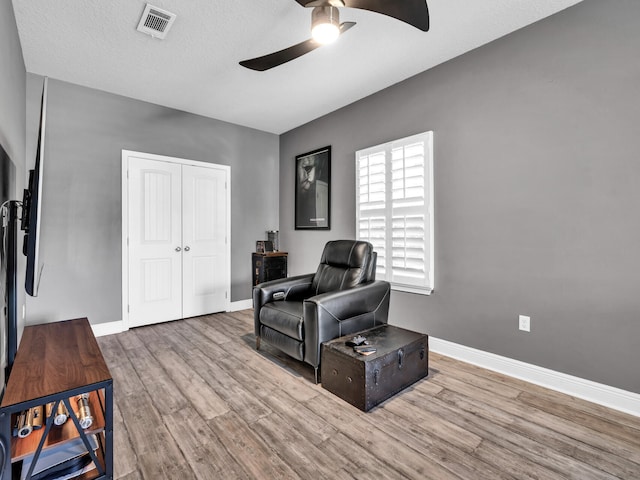 living area with wood finished floors, ceiling fan, visible vents, and baseboards