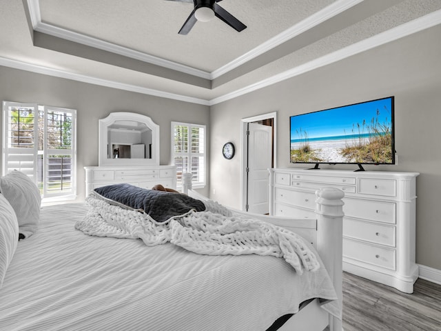bedroom with light wood-type flooring, a raised ceiling, a textured ceiling, and crown molding