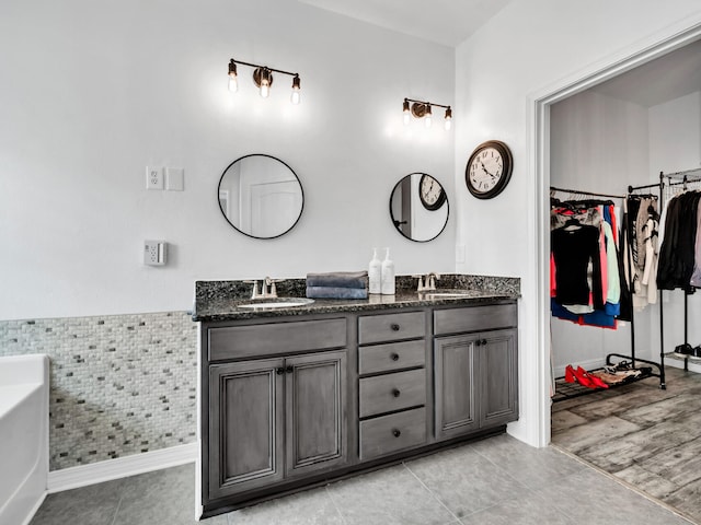 full bath featuring a spacious closet, a wainscoted wall, double vanity, and a sink