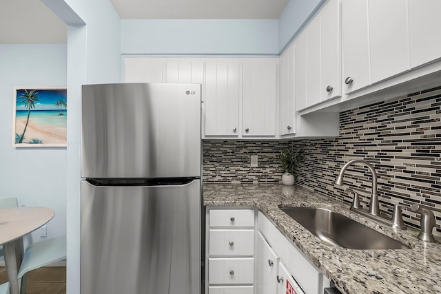 kitchen featuring light stone counters, white cabinets, a sink, freestanding refrigerator, and backsplash