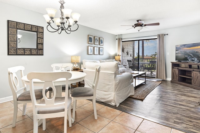 dining room featuring baseboards, light wood-type flooring, ceiling fan with notable chandelier, and a textured ceiling