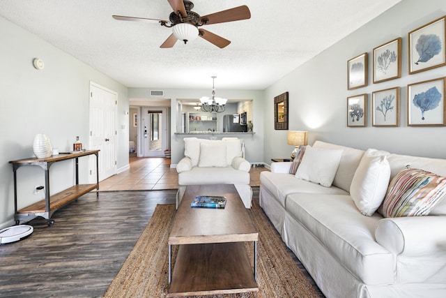living area featuring visible vents, baseboards, a textured ceiling, wood finished floors, and ceiling fan with notable chandelier