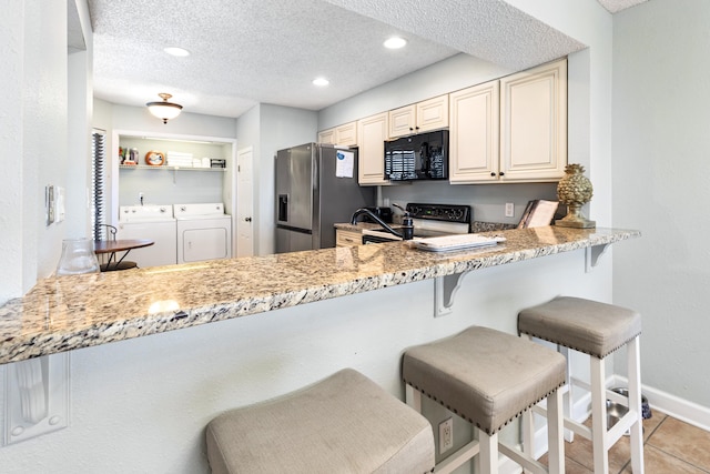 kitchen with electric range oven, cream cabinets, black microwave, washer and dryer, and stainless steel fridge with ice dispenser