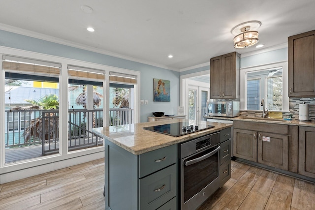 kitchen featuring crown molding, a sink, appliances with stainless steel finishes, a kitchen island, and light wood finished floors
