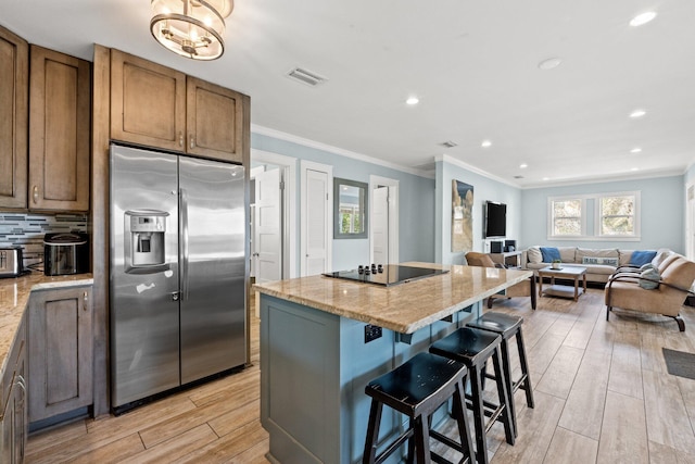 kitchen featuring black electric stovetop, visible vents, a kitchen island, ornamental molding, and stainless steel fridge with ice dispenser