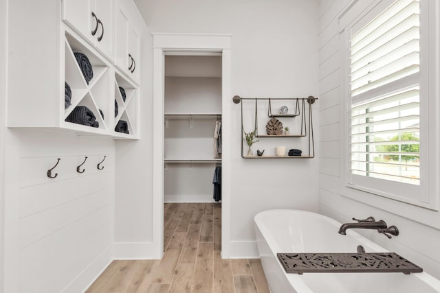 full bathroom featuring wood finished floors, baseboards, a walk in closet, and a freestanding bath