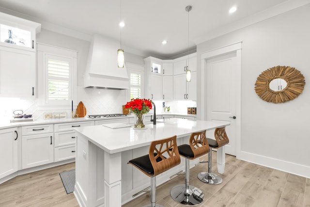 kitchen featuring a kitchen breakfast bar, tasteful backsplash, light countertops, premium range hood, and light wood finished floors