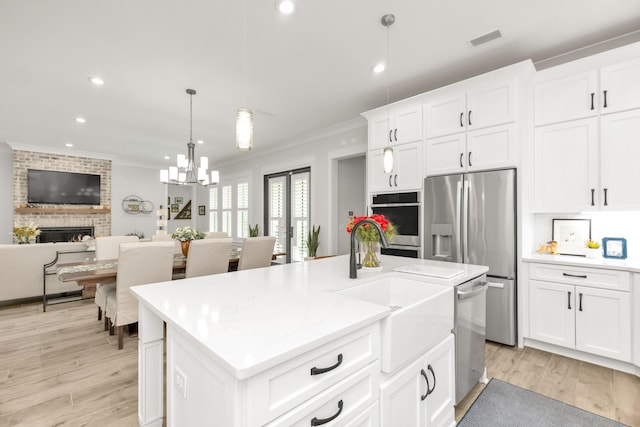 kitchen featuring visible vents, appliances with stainless steel finishes, a fireplace, a sink, and ornamental molding