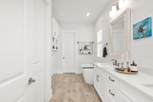 full bath featuring double vanity, wood finished floors, recessed lighting, a freestanding bath, and a sink