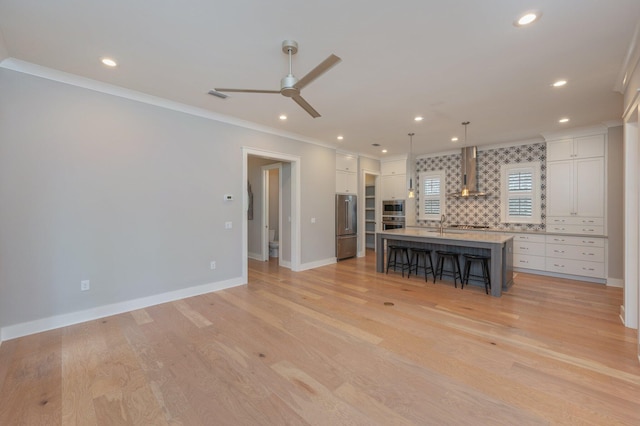 kitchen with a kitchen bar, ornamental molding, stainless steel appliances, white cabinetry, and an island with sink