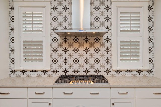 kitchen with wall chimney range hood, white cabinetry, light stone countertops, and stainless steel gas cooktop
