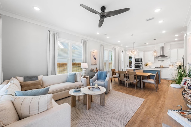 living area featuring a ceiling fan, crown molding, light wood finished floors, recessed lighting, and a chandelier