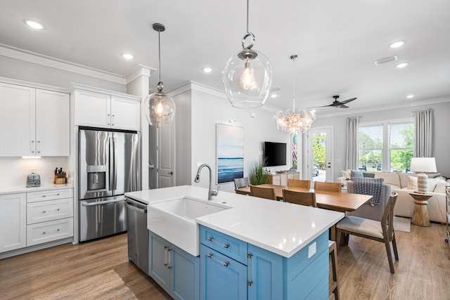 kitchen with stainless steel appliances, open floor plan, a sink, crown molding, and white cabinetry