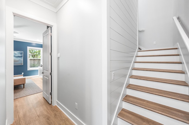 staircase with wood finished floors, ornamental molding, and baseboards