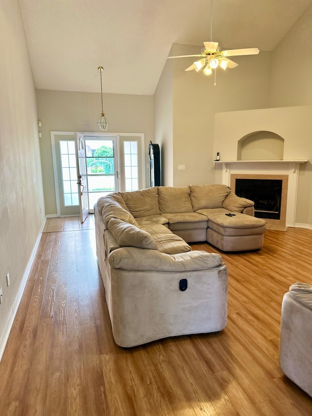 living room featuring a fireplace, ceiling fan, vaulted ceiling, baseboards, and wood finished floors