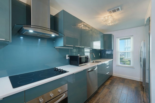 kitchen featuring wall chimney range hood, a sink, appliances with stainless steel finishes, light countertops, and dark wood-style flooring