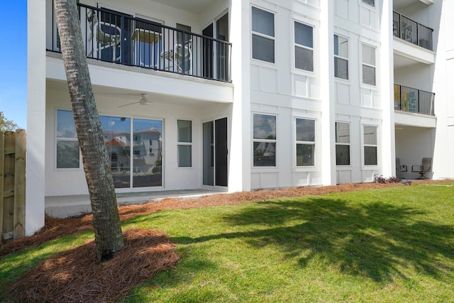 back of property with stucco siding, a ceiling fan, a yard, and a balcony