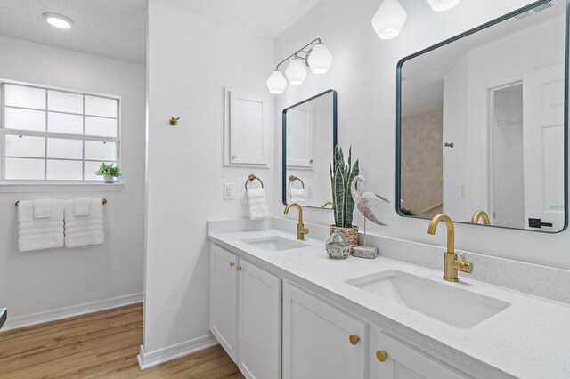 full bath with a sink, baseboards, double vanity, and wood finished floors