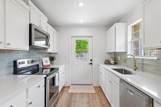 kitchen with a textured ceiling, appliances with stainless steel finishes, light wood-type flooring, a sink, and light countertops