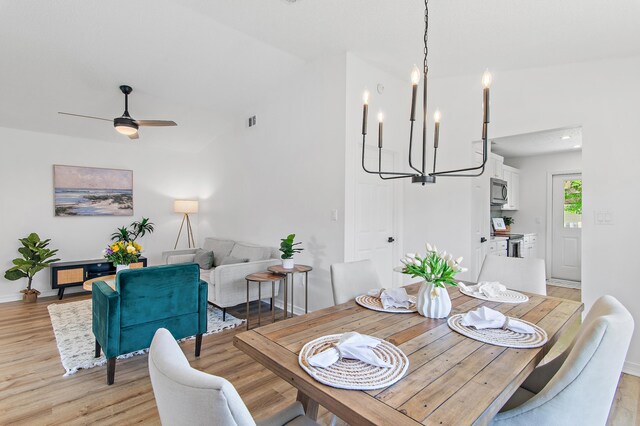 dining area with visible vents, baseboards, ceiling fan with notable chandelier, lofted ceiling, and light wood-style flooring