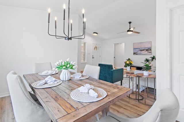 dining area with light wood-type flooring, baseboards, ceiling fan with notable chandelier, and lofted ceiling
