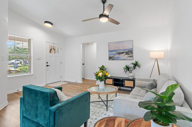 living room with baseboards, ceiling fan, lofted ceiling, and light wood-type flooring