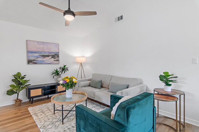 living room featuring ceiling fan, visible vents, vaulted ceiling, wood finished floors, and baseboards