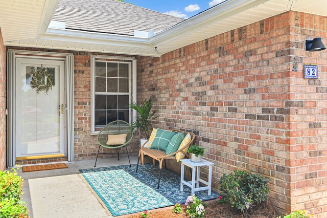 doorway to property with a shingled roof and brick siding