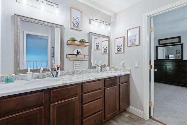 bathroom with a textured wall, double vanity, a sink, and wood finished floors