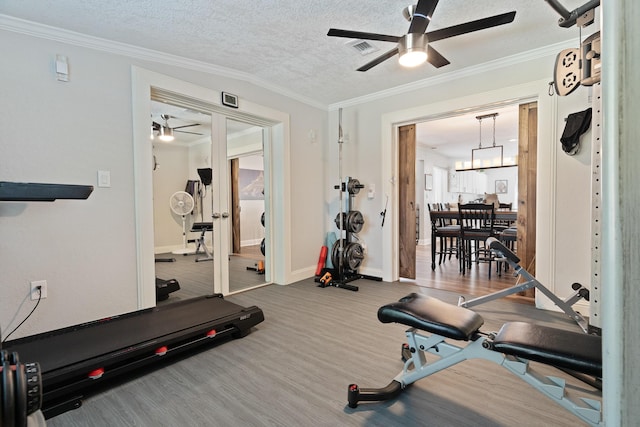 exercise area featuring a ceiling fan, ornamental molding, visible vents, and a textured ceiling