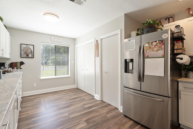 kitchen featuring wood finished floors, stainless steel fridge with ice dispenser, white cabinetry, visible vents, and baseboards