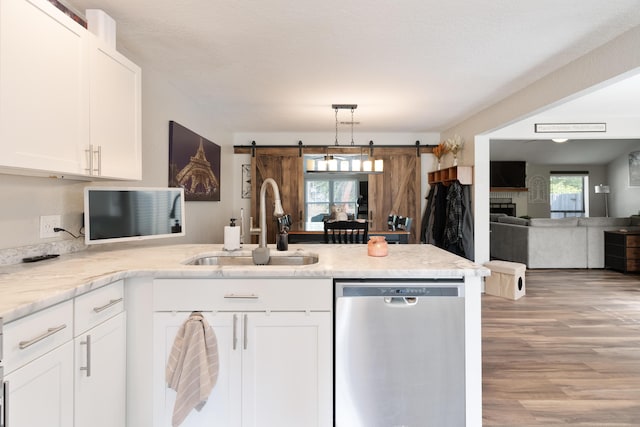 kitchen with a sink, a peninsula, a barn door, white cabinets, and stainless steel dishwasher