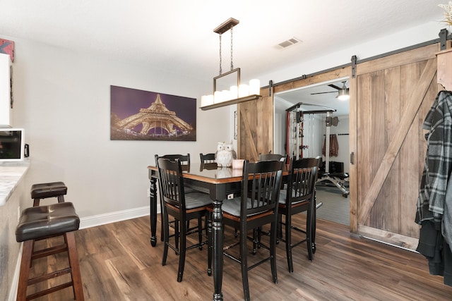 dining room featuring wood finished floors, visible vents, a barn door, and baseboards