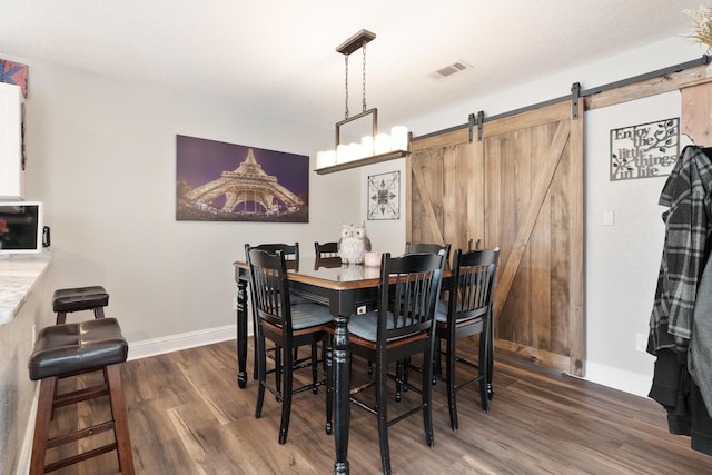 dining space featuring baseboards, visible vents, a barn door, and wood finished floors