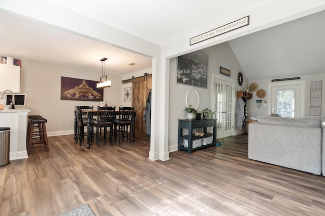 living area featuring light wood-style flooring, french doors, baseboards, a barn door, and vaulted ceiling