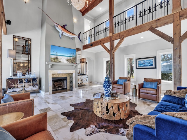 living room featuring a tiled fireplace, ornamental molding, marble finish floor, and a towering ceiling