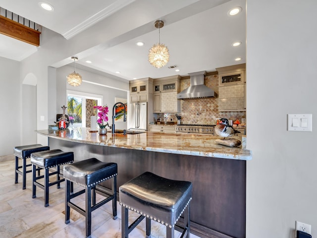 kitchen featuring a sink, tasteful backsplash, high quality appliances, a peninsula, and wall chimney range hood