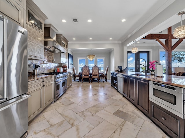 kitchen featuring wall chimney range hood, a sink, appliances with stainless steel finishes, visible vents, and a notable chandelier