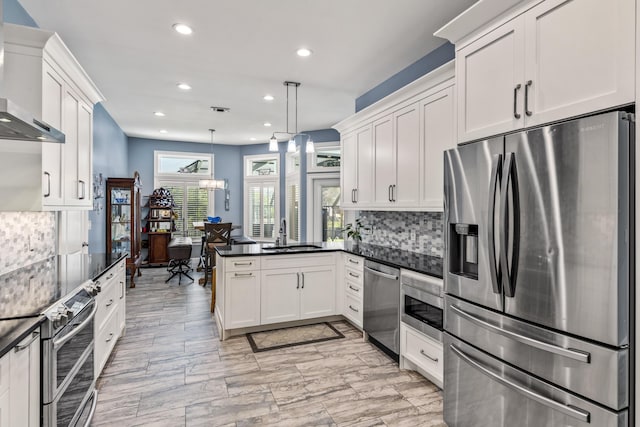 kitchen with appliances with stainless steel finishes, a sink, wall chimney exhaust hood, a peninsula, and recessed lighting