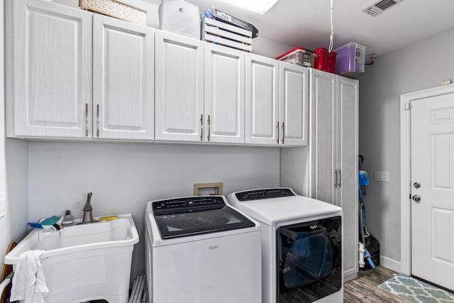 clothes washing area with visible vents, wood finished floors, separate washer and dryer, a sink, and cabinet space