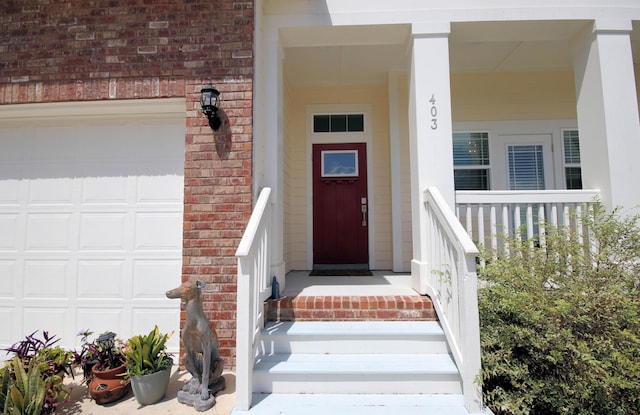 doorway to property with covered porch, an attached garage, and brick siding