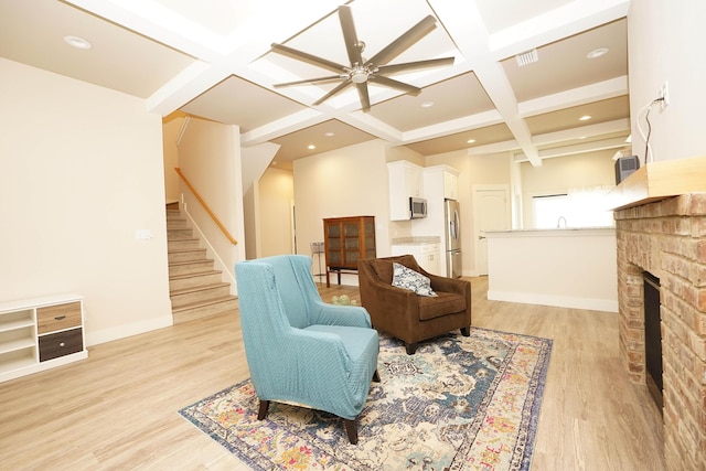 living area featuring a ceiling fan, beamed ceiling, coffered ceiling, stairs, and light wood-style flooring