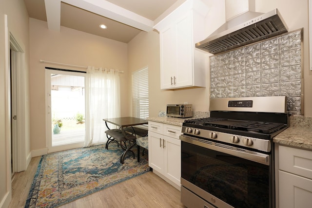 kitchen featuring light wood-type flooring, wall chimney exhaust hood, stainless steel gas range oven, and white cabinets