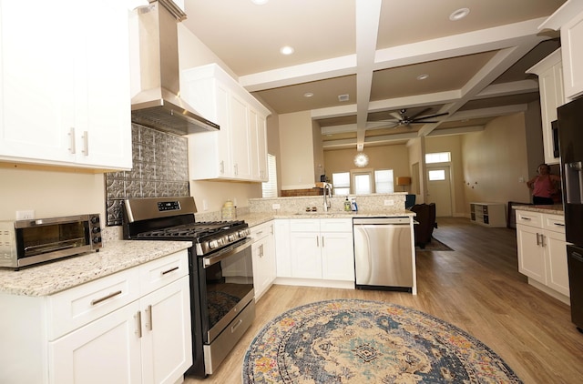 kitchen featuring a peninsula, wall chimney range hood, a ceiling fan, coffered ceiling, and stainless steel appliances