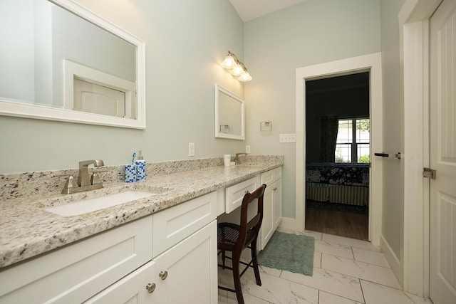 ensuite bathroom with double vanity, marble finish floor, ensuite bathroom, baseboards, and a sink