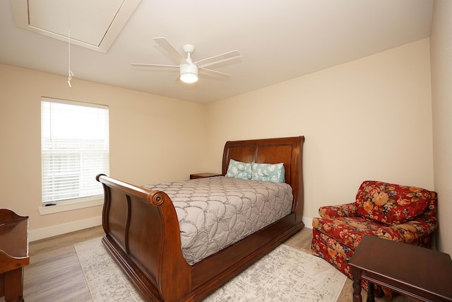 bedroom featuring light wood-type flooring, attic access, baseboards, and a ceiling fan