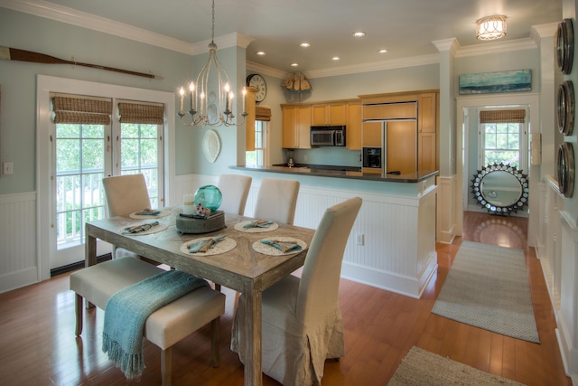 dining space with crown molding, an inviting chandelier, wainscoting, a decorative wall, and light wood-style floors