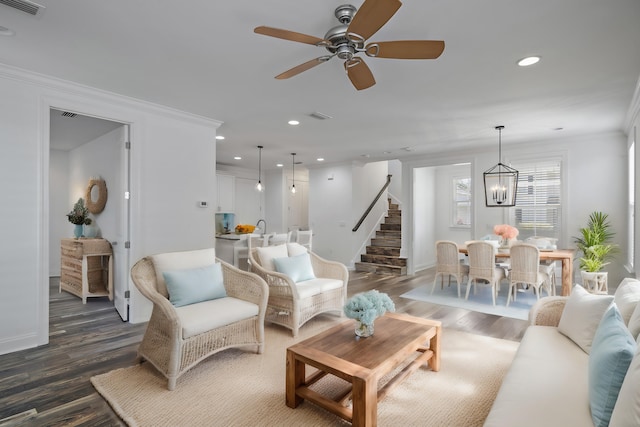 living area with crown molding, stairs, ceiling fan with notable chandelier, recessed lighting, and dark wood-type flooring